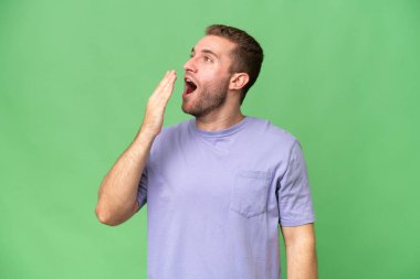 Yeşil krom arka planda izole edilmiş yakışıklı beyaz adam esniyor ve ağzını eliyle açık tutuyor.