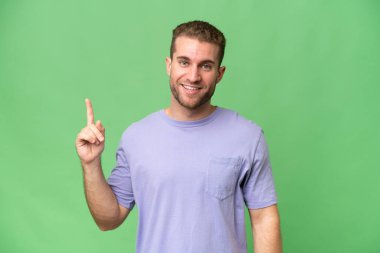 Yeşil krom arka planda izole edilmiş yakışıklı beyaz adam en iyinin işareti olarak parmağını kaldırıyor ve gösteriyor.