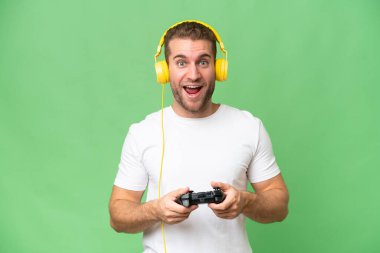 Yeşil krom arka planda izole edilmiş bir video oyunu kontrolörüyle oynayan genç yakışıklı adam.