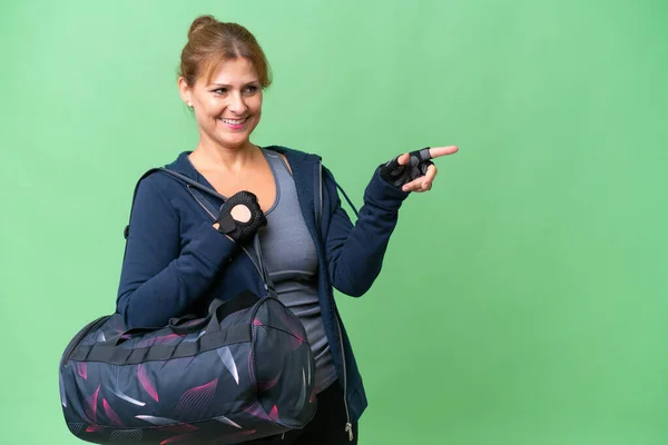 脇に指を指して製品を提示孤立背景にスポーツバッグを持つ中高年のスポーツ女性 — ストック写真
