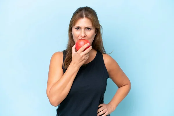 青の背景に隔離された中年の白人女性がリンゴを食べる — ストック写真