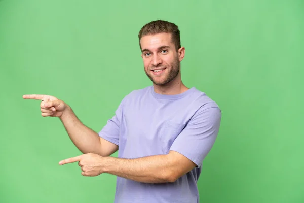 緑のクロマを背景に指を横に向けて製品を提示若いハンサムな白人男性 — ストック写真