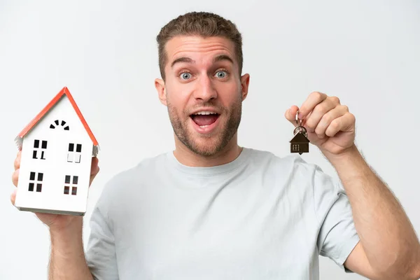 stock image Young caucasian man holding home keys and toy house isolated on white background