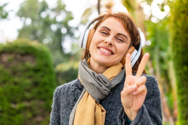 Μπρουνέτ Γυναίκα Ακούγοντας Μουσική Ακουστικά Εξωτερικούς Χώρους Χαμογελώντας Και Δείχνοντας — Φωτογραφία Αρχείου