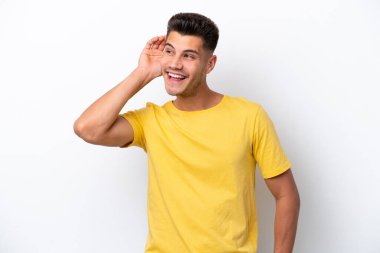 Beyaz arka planda izole edilmiş genç beyaz bir adam. Kulağına elini sürerek bir şeyler dinliyor.