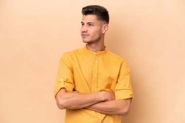 Young caucasian man isolated on beige background looking to the side