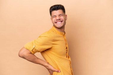 Beyazlı genç bir adam bej arka planda izole edilmiş. Çaba gösterdiği için sırt ağrısı çekiyor.