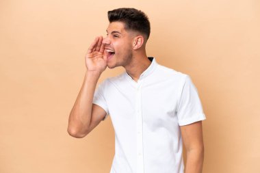 Young caucasian man isolated on beige background shouting with mouth wide open to the side