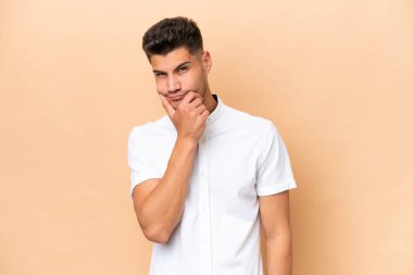 Beyazlı genç bir adam bej arka planda izole edilmiş. Şüpheleri var.