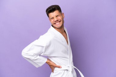 Mor arka planda karate yapan genç beyaz adam gayret gösterdiği için sırt ağrısı çekiyor.