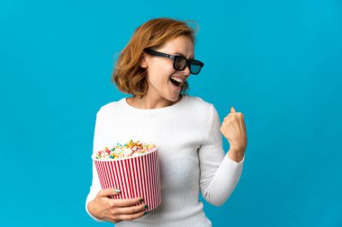 Genç Gürcü bir kadın mavi arka planda gözlüklü ve elinde koca bir kova patlamış mısırla yan tarafa bakıyor.