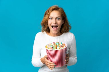 Genç Gürcü bir kadın mavi arka planda izole edilmiş. Elinde koca bir kova patlamış mısır var.