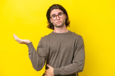 Caucasian handsome man isolated on yellow background having doubts
