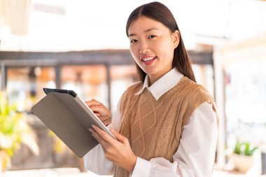 Dışarıdaki genç Çinli kadın tablet ekranına mutlu bir ifadeyle dokunuyor.