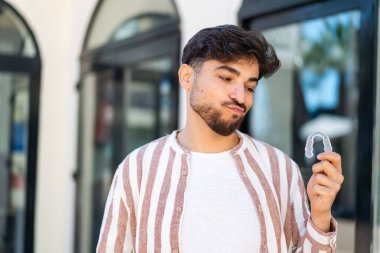 Yakışıklı bir Arap 'ın görünmeyen diş tellerini açık havada tutması hüzünlü bir ifade.