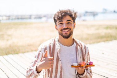 Yakışıklı bir Arap açık havada sashimi tutuyor. Başparmakları havada. Çünkü iyi bir şey oldu.