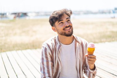 Açık havada kornet dondurmalı yakışıklı bir Arap gülümserken yukarı bakıyor.