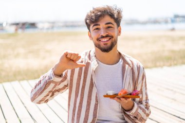 Yakışıklı bir Arap açık havada saşimi tutuyor gururlu ve kendinden memnun.