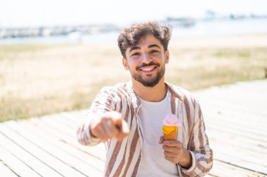 Açık havada kornet dondurmalı yakışıklı bir Arap, kendine güvenen bir ifadeyle seni işaret ediyor.