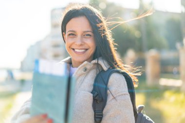 Açık havada elinde mutlu bir ifadeyle pasaport tutan genç bir kadın.