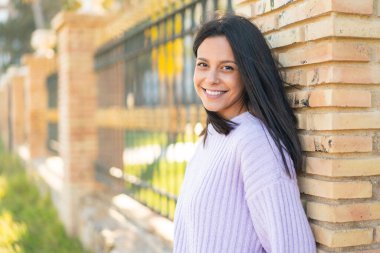 Açık havada genç bir kadın kollarını ön cephede kavuşturuyor.