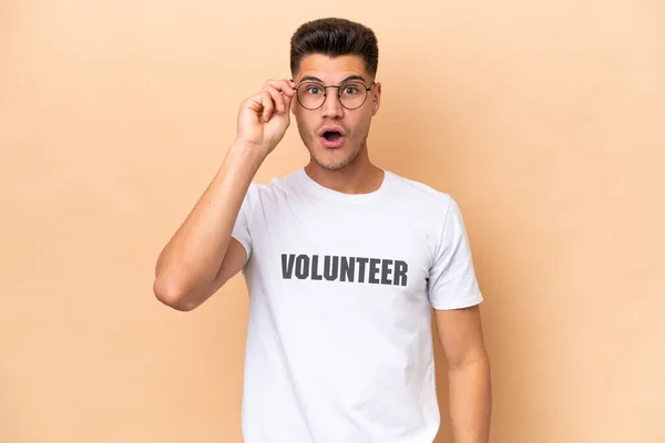 Joven Voluntario Caucásico Aislado Sobre Fondo Beige Con Gafas Sorprendido —  Fotos de Stock