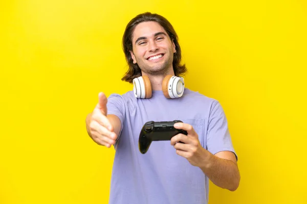 若いですハンサムなCaucasian男遊びますとともにAビデオゲームコントローラ上の隔離された上に黄色の背景揺れ手のために閉じますA良い取引 — ストック写真