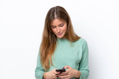 Beyaz arka planda izole edilmiş genç beyaz kadın cep telefonuyla mesaj gönderiyor.