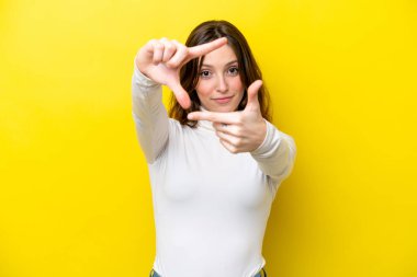 Sarı arka planda izole edilmiş, odaklanan genç beyaz bir kadın. Çerçeve sembolü