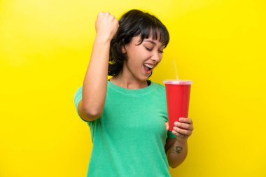 Sarı arka planda gazoz tutan genç Arjantinli kadın zaferi kutluyor.