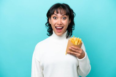 Arjantinli genç bir kadın elinde kızarmış cipslerle mavi arka planda sürpriz bir yüz ifadesiyle izole edilmiş.