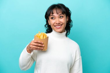 Elinde kızarmış cips tutan genç Arjantinli kadın mavi arka planda izole edilmiş bir şekilde yukarı bakarken bir fikir düşünüyor.