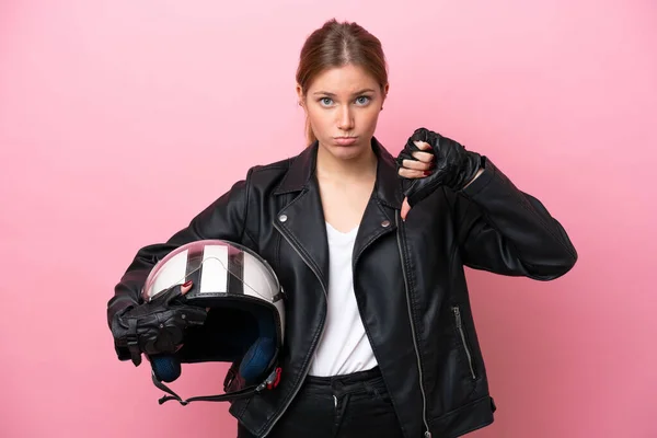 Young caucasian woman with a motorcycle helmet isolated on pink background showing thumb down with negative expression