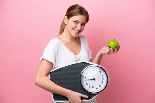 stock image Young caucasian woman isolated on pink background with weighing machine and with an apple