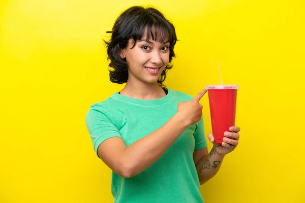 年轻的阿根廷女人拿着苏打水 背景是黄色的 指向后方 — 图库照片