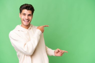 İzole edilmiş geçmişi olan beyaz, yakışıklı genç bir adam. Parmakla göstererek bir ürün sunuyor.