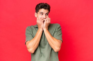 Genç, beyaz, yakışıklı, kırmızı arka planda izole edilmiş gergin ve korkmuş bir adam elleriyle suni teneffüs yapıyor.