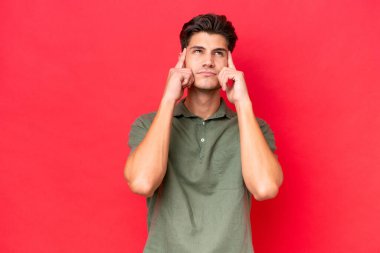 Genç, beyaz, yakışıklı bir adam kırmızı arka planda izole edilmiş. Şüpheleri ve düşünceleri var.