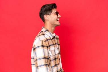 Beyaz tenli yakışıklı, kırmızı arka planda izole edilmiş. Yan pozisyonda gülüyor.