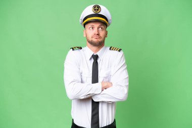 Uçak pilotu izole edilmiş arka planda, omuzlarını kaldırırken şüphe jesti yapıyor.