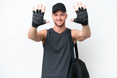 İzole edilmiş beyaz arka planda spor çantalı genç sarışın beyaz adam parmaklarıyla 10 kişi sayıyor.