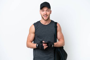 İzole edilmiş beyaz arka plan üzerinde spor çantalı genç sarışın beyaz adam şaşırdı ve bir mesaj gönderiyor.