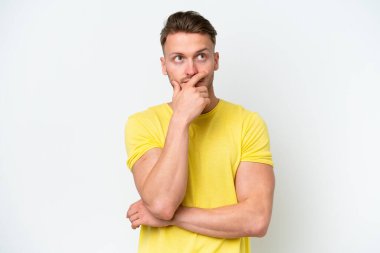 Beyaz arka planda izole edilmiş genç, sarışın ve kafası karışmış bir adam.