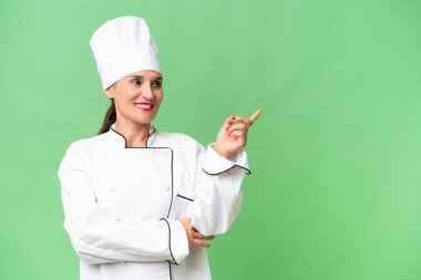 Orta yaşlı aşçı kadın izole edilmiş arka planda parmak göstererek bir ürün sunuyor.