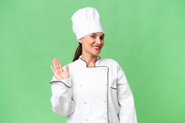 Orta yaşlı aşçı kadın, izole bir arka planda, mutlu bir ifadeyle selamlıyor.