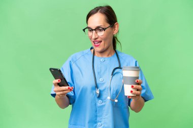 Orta yaşlı bir hemşire, izole edilmiş bir geçmişi var. Elinde kahve ve cep telefonu var.