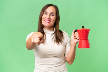 Kafkasyalı orta yaşlı bir kadın izole edilmiş arka planda kahve makinesini tutarken kendine güvenen bir ifadeyle sana işaret ediyor.