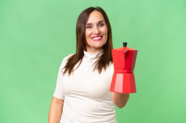 Orta yaşlı, beyaz bir kadın elinde kahve fincanı tutarken mutlu bir ifade takınıyor.