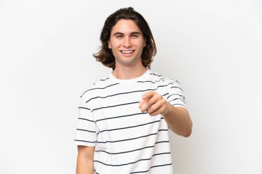 Beyaz arka planda soyutlanmış yakışıklı genç adam şaşırmış ve ön tarafı işaret ediyor.