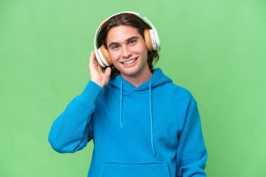 Genç yakışıklı adam yeşil renkli arka planda izole edilmiş müzik dinliyor.